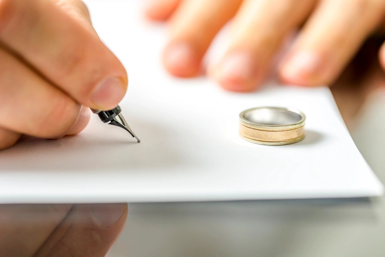 A person signing papers with a wedding ring on top of it.
